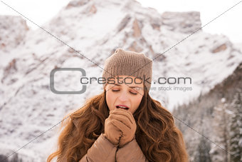 Woman warming hands with breathe among snow-capped mountains