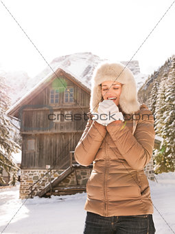 Happy woman blowing warm breath on hands near mountain house