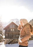 Happy young woman standing in the front of a cosy mountain house