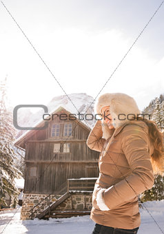 Happy young woman standing in the front of a cosy mountain house