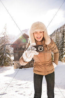 Woman standing near mountain house and taking photos with camera