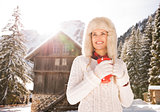 Smiling woman with red cup standing near cosy mountain house