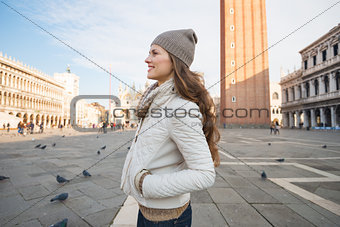 Happy young woman standing on Piazza San Marco and looking aside