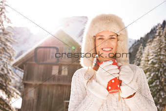 Young woman with red cup standing near cosy mountain house