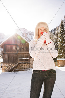 Woman enjoying hot beverage while standing near mountain house