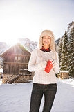 Happy woman with red cup standing near cosy mountain house