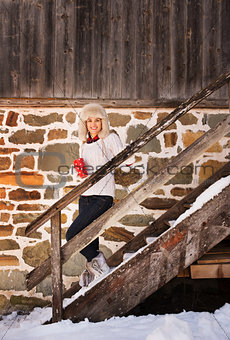 Smiling woman with cup standing on stairs of cosy mountain house