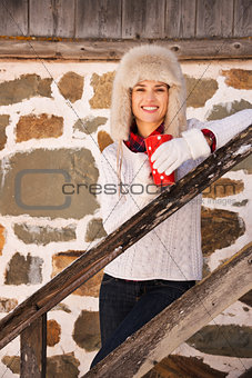 Happy woman with cup standing on stairs of cosy mountain house