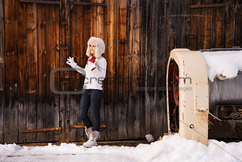 Woman in furry hat holding red cup in front of rustic wood wall