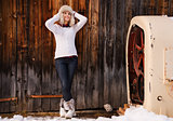 Relaxed young woman in furry hat standing near rustic wood wall