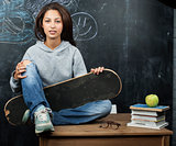 young cute teenage girl in classroom at blackboard seating on table smiling
