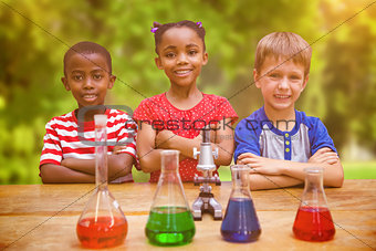Composite image of cute pupils standing with arms crossed behind beaker