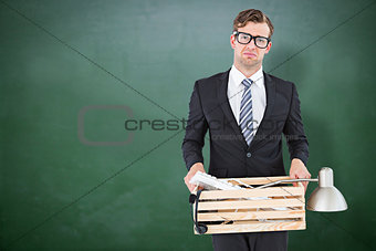 Composite image of sad geeky businessman holding box of his things