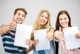 Composite image of students holding up exam and doing thumbs up