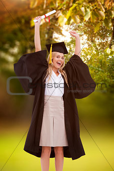 Composite image of blonde student in graduate robe holding up her diploma