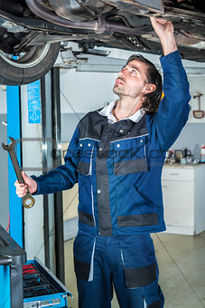 Mechanic repairing a lifted car with big wrench