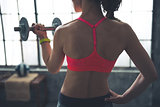 Seen from behind fitness woman lifting dumbbell in loft gym