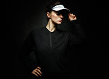 Woman athlete adjusting tennis visor against dark background