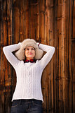 Relaxed woman in knitted sweater and furry hat near wood wall