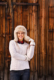 Woman in white knitted sweater and furry hat near wood wall