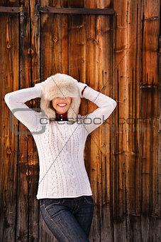 Young woman pulled furry hat over her eyes near rustic wood wall