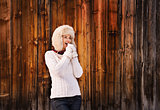 Smiling woman blowing warm breath on her hands near wood wall