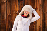 Young woman pulled furry hat over her eyes near rustic wood wall