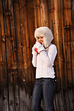 Happy woman in furry hat with red cup near rustic wood wall