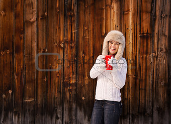Happy woman in knitted sweater with cup near rustic wood wall