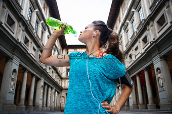 Sporty woman with headset is drinking water from the bottle