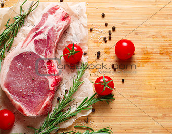 Pieces of crude meat with rosemary and tomatoes.