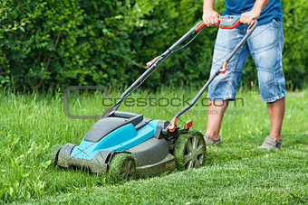 Man mowing the lawn with blue lawnmower in summertime