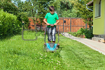 Boy cutting grass around the house in summertime