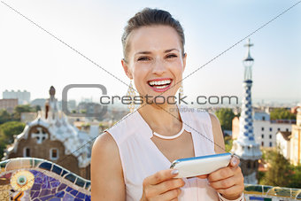 Smiling woman writing sms on smartphone in Park Guell, Barcelona