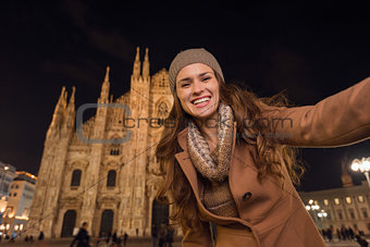 Smiling young woman taking selfie in front of Duomo in evening