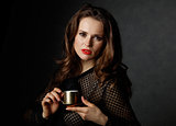 Portrait of woman holding cup of coffee against dark background