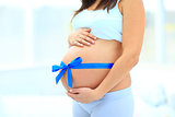 woman holds her baby bump, tied with a blue bow