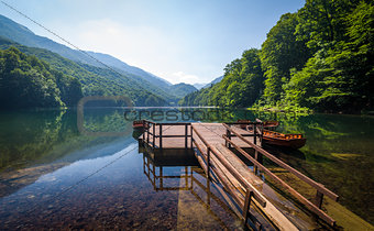 Calm lake water with reflections of forest on the hills and beautiful old wooden pier