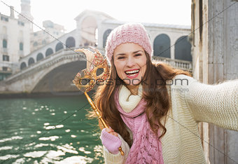 Smiling woman with Venice Mask near Rialto Bridge taking selfie