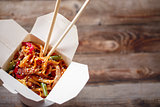 Noodles with pork and vegetables in take-out box on wooden table
