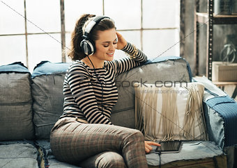 Happy young woman in headphones choosing track on tablet PC