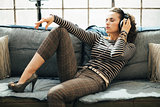 Woman laying on couch and listening to music in loft apartment