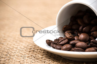 White coffeecup and plate with spilled coffeebeans