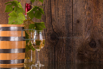 Glass of wine with barrel white bottle behind grapeleaves
