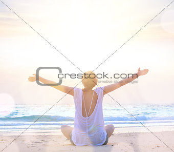 woman with hands up at sunrise beach