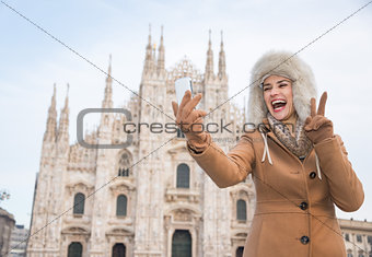 Woman tourist showing victory gesture and taking selfie in Milan
