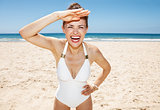 Cheerful woman in white swimsuit at sandy beach on sunny day