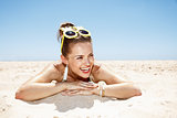 Smiling woman in swimsuit and pineapple glasses laying on beach