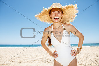 Happy woman in white swimsuit and straw hat at sandy beach