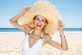 Smiling woman in swimsuit playing with big straw hat at beach